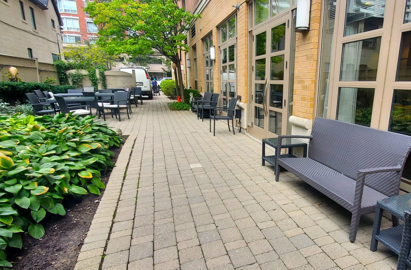 Clean patio stones well maintained next to flower bed full of annuals. Creeping plants make its way up the pergola behind the outdoor seating area.